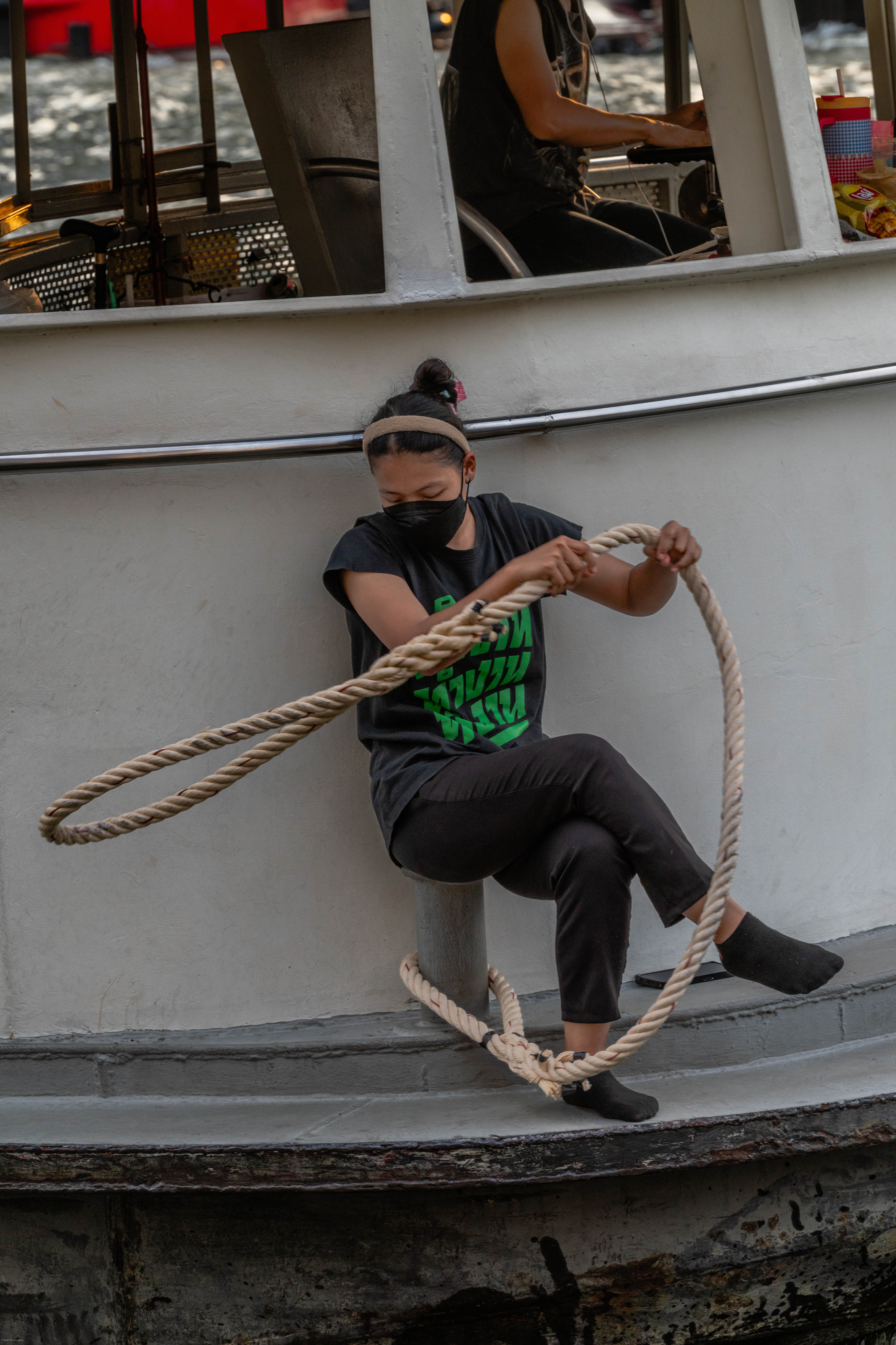 Girl on boat tossing hawser toward mooring bollard.