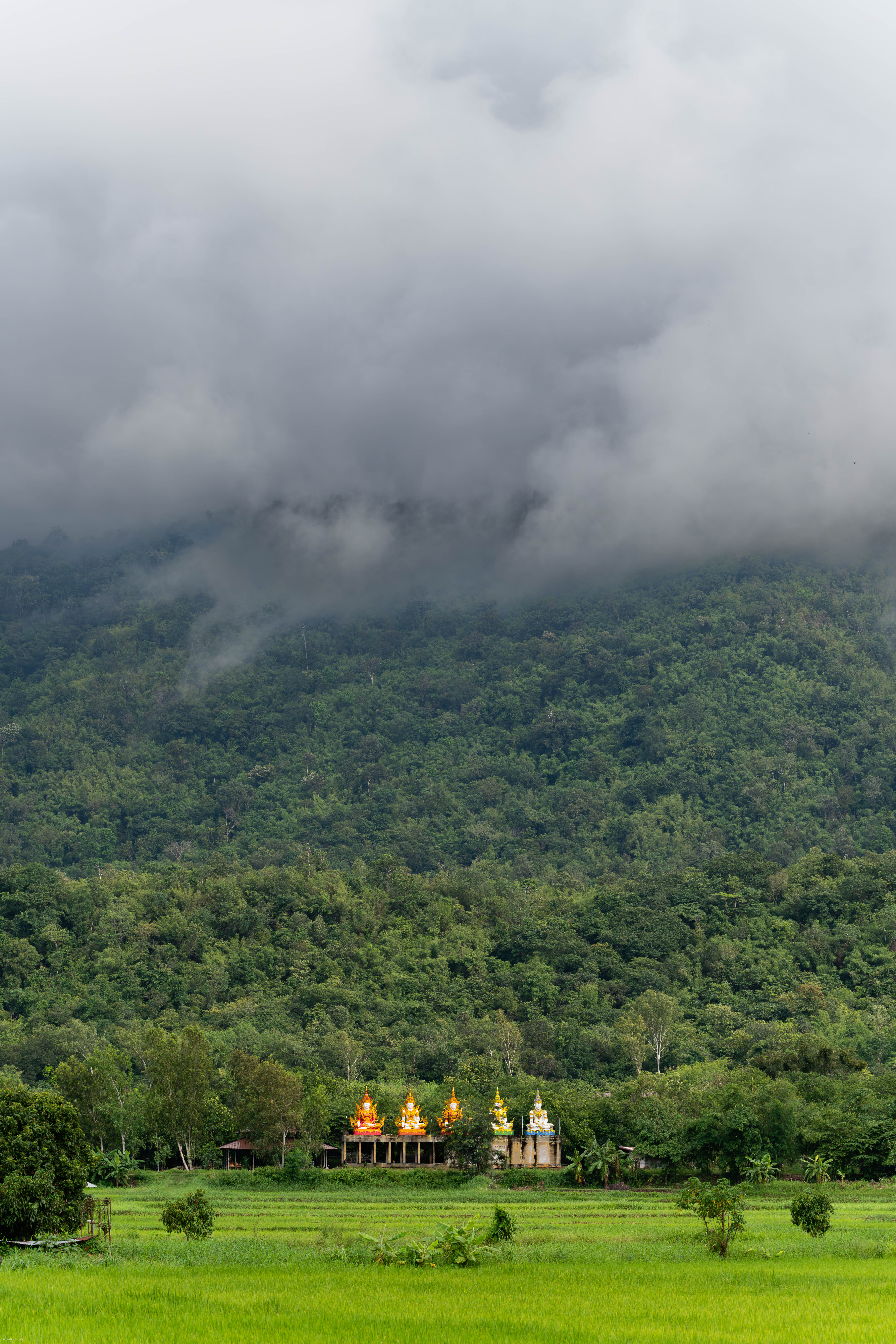 Buddhist monuments before a mountain topped with clouds.